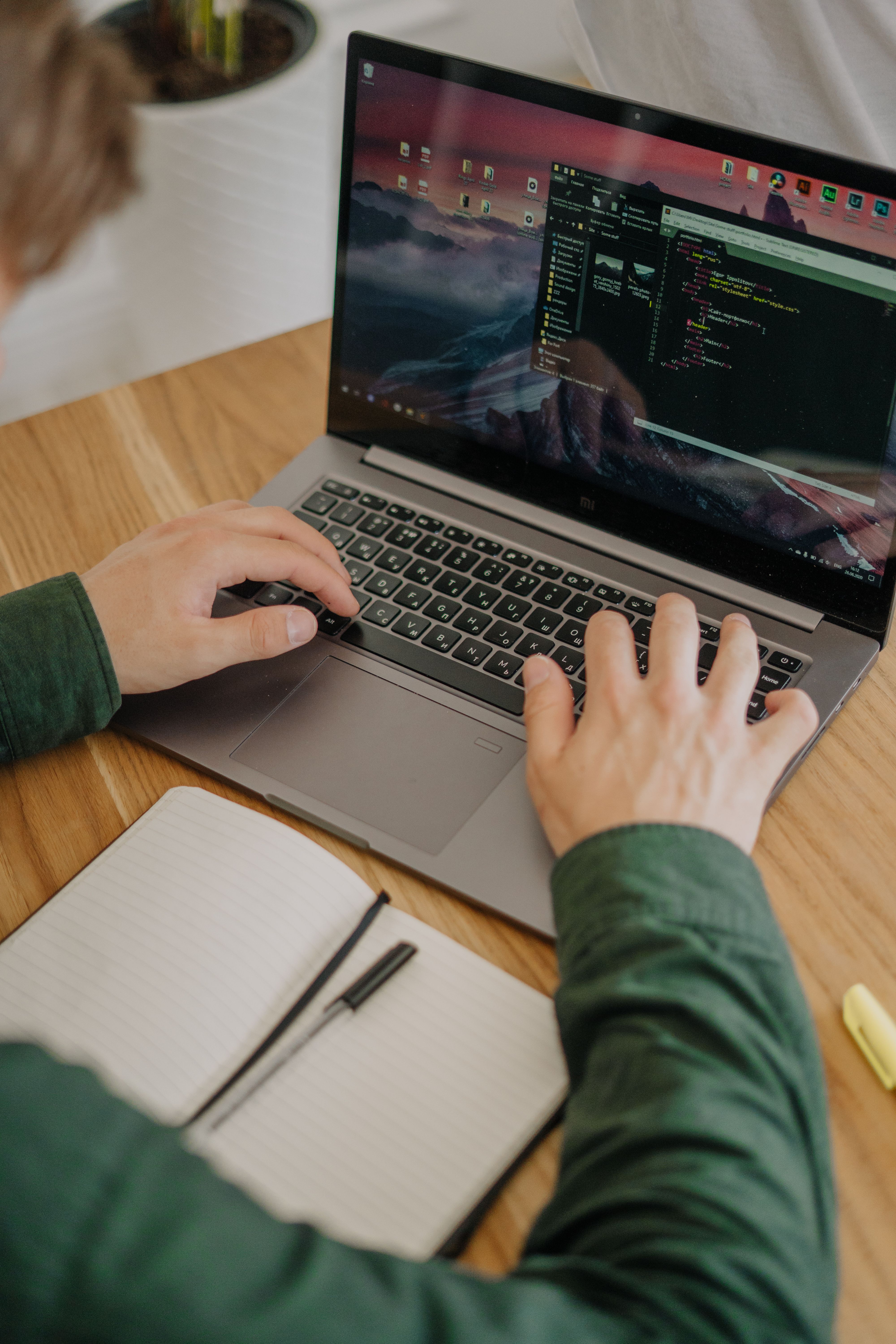 Hands typing code on a laptop beside an open notebook